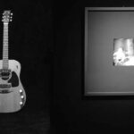 Kurt Cobain's 1959 Martin D 18E on exhibition pictured next to a photo of Cobain playing the guitar.